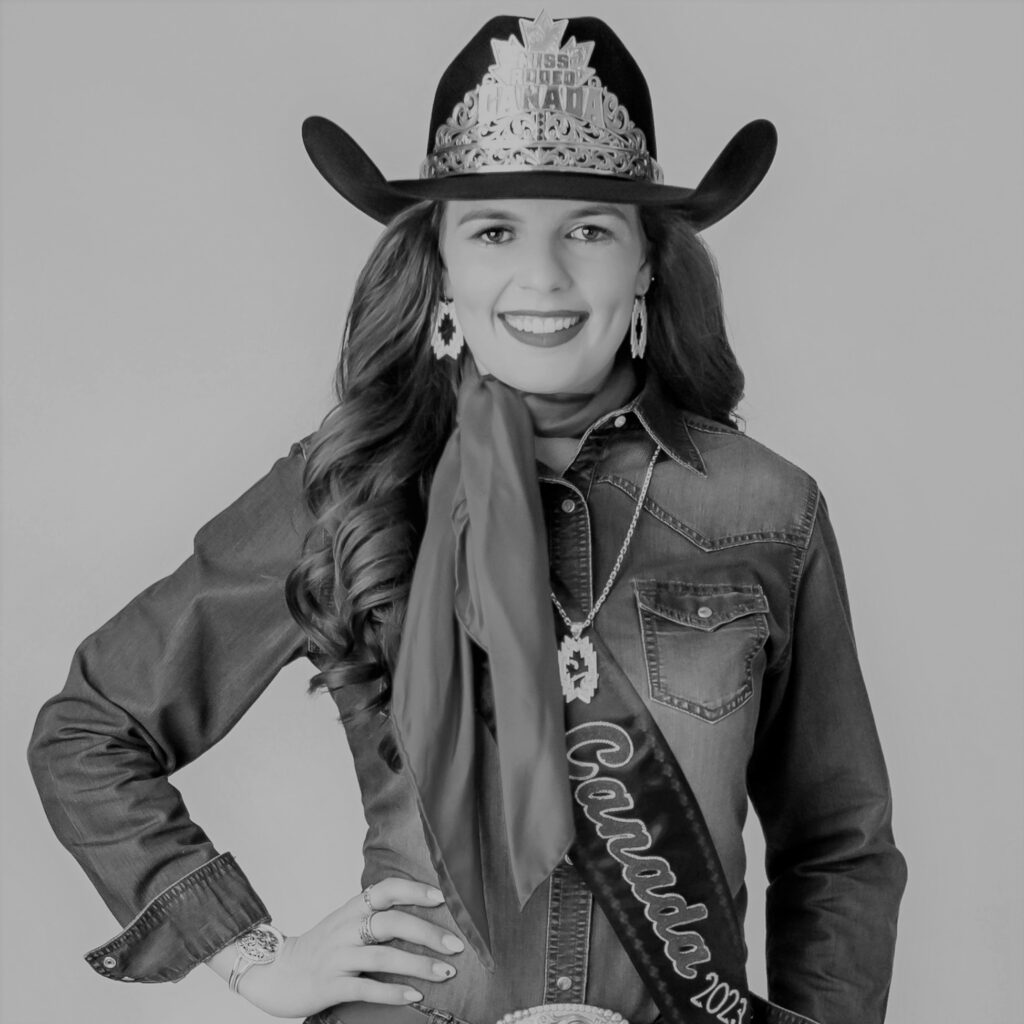 A black and white photo of Mackenzie Skeels standing in a cowboy hat with long dark hair, wearing a jean jacket and a sash across her chest that reads "Canada". Her hat says "Miss Rodeo Canada".
